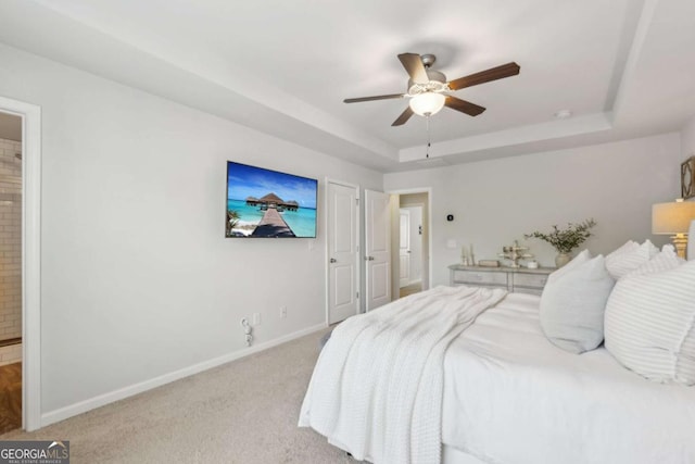 bedroom featuring baseboards, a tray ceiling, light carpet, a ceiling fan, and ensuite bath