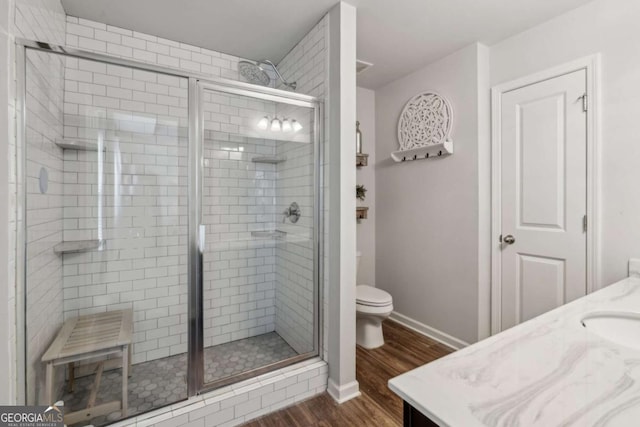 bathroom featuring wood finished floors, vanity, a shower stall, toilet, and baseboards