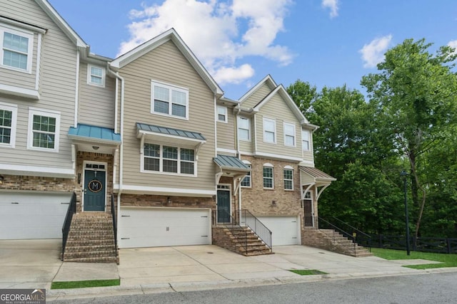 townhome / multi-family property with a garage, concrete driveway, a standing seam roof, brick siding, and metal roof