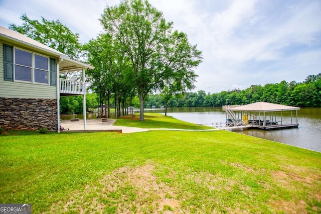 view of grassy yard with a water view, a dock, and a patio area
