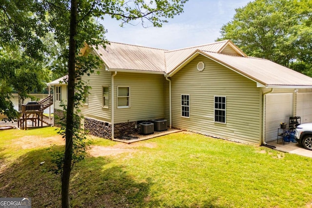 rear view of house with a garage, a yard, central air condition unit, and metal roof