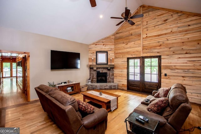 living room with wood walls, high vaulted ceiling, ceiling fan, light wood-type flooring, and french doors