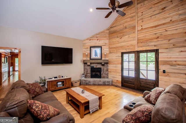 living area with wooden walls, french doors, light wood-style floors, a ceiling fan, and a fireplace