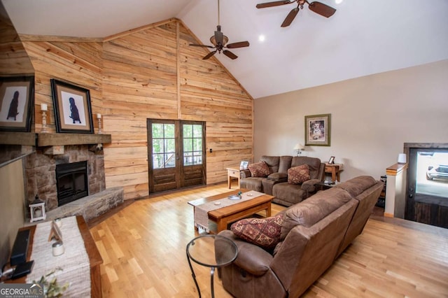 living room with wood walls, wood finished floors, french doors, a ceiling fan, and high vaulted ceiling