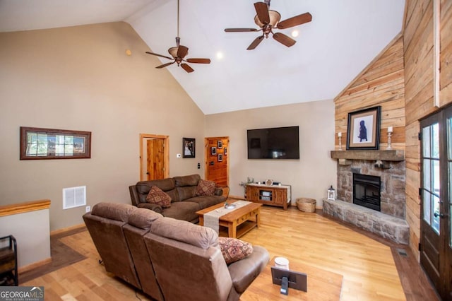 living area featuring high vaulted ceiling, wood finished floors, a stone fireplace, ceiling fan, and baseboards