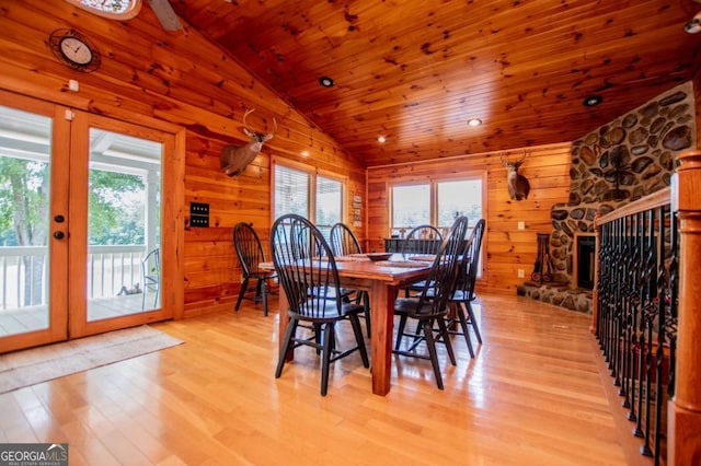 dining area featuring vaulted ceiling, wooden ceiling, light wood finished floors, a fireplace, and wooden walls