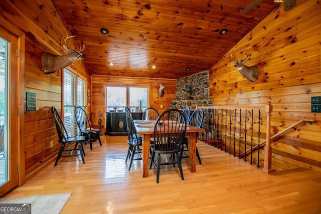 dining space featuring lofted ceiling, light wood finished floors, wooden ceiling, and wood walls
