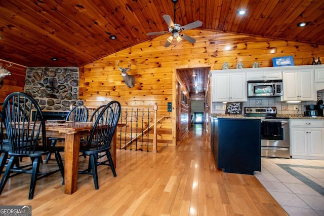 dining space with vaulted ceiling, wood ceiling, wooden walls, a ceiling fan, and light wood finished floors