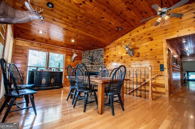 dining room featuring wooden walls, wood ceiling, lofted ceiling, wood finished floors, and ceiling fan