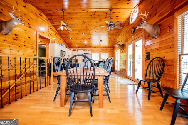 dining space with lofted ceiling, a ceiling fan, light wood-style floors, wood ceiling, and wooden walls