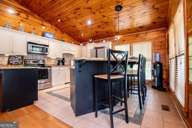 kitchen with appliances with stainless steel finishes, lofted ceiling, wooden ceiling, backsplash, and white cabinets