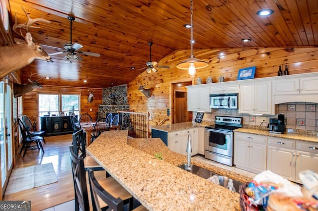 kitchen featuring stainless steel appliances, wood walls, vaulted ceiling, a ceiling fan, and wooden ceiling