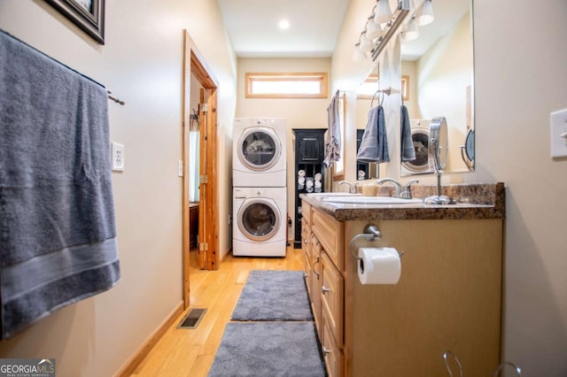 bathroom with stacked washer / dryer, wood finished floors, vanity, and baseboards