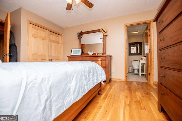 bedroom with light wood finished floors, ensuite bath, a ceiling fan, a closet, and baseboards