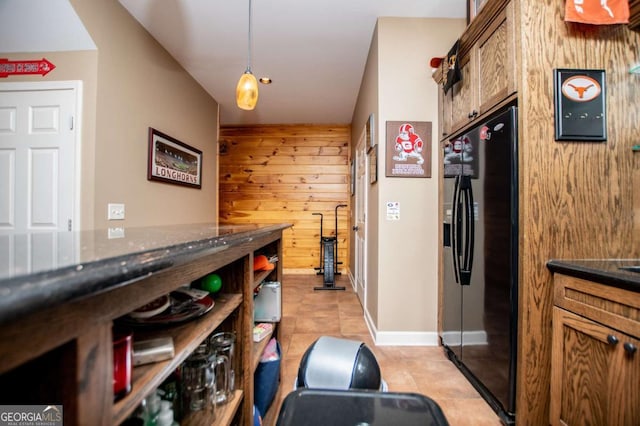 kitchen with black refrigerator with ice dispenser, wood walls, light tile patterned floors, hanging light fixtures, and brown cabinetry