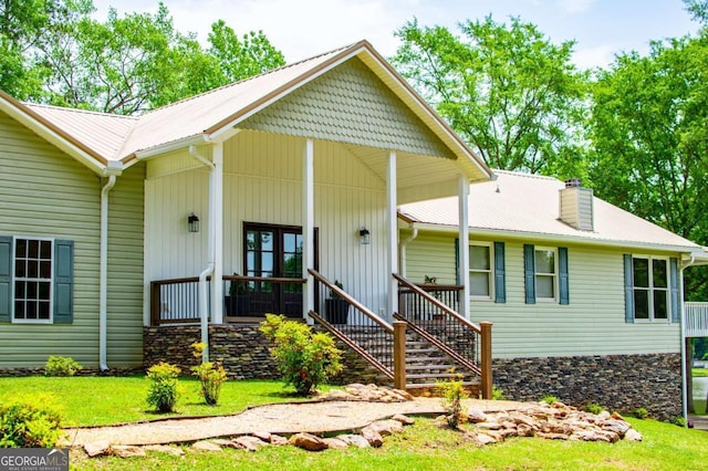 view of front facade with a porch, a chimney, a front yard, metal roof, and stairs