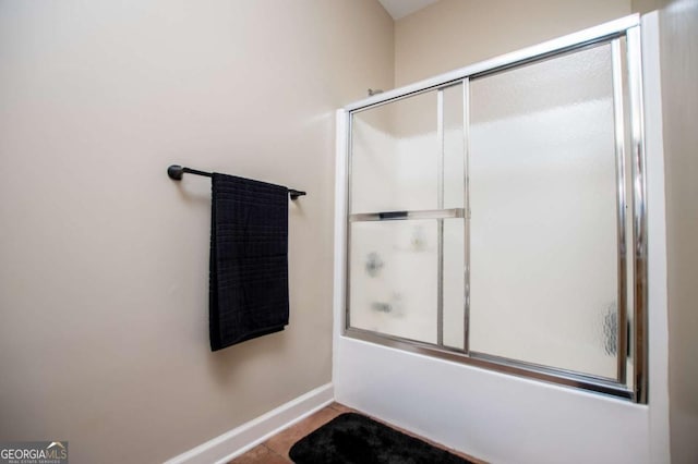 bathroom featuring bath / shower combo with glass door and baseboards