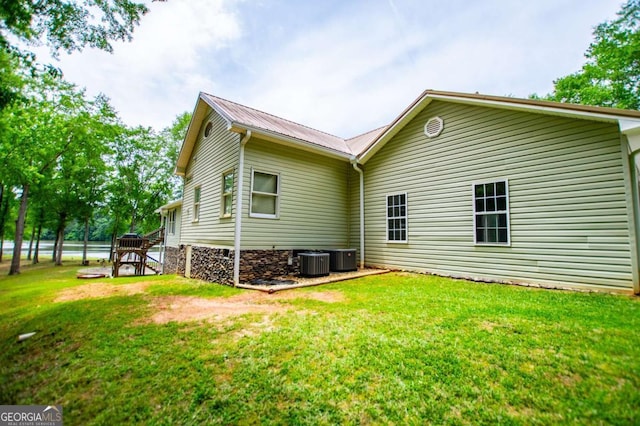 rear view of house with central AC, metal roof, a yard, and stairs