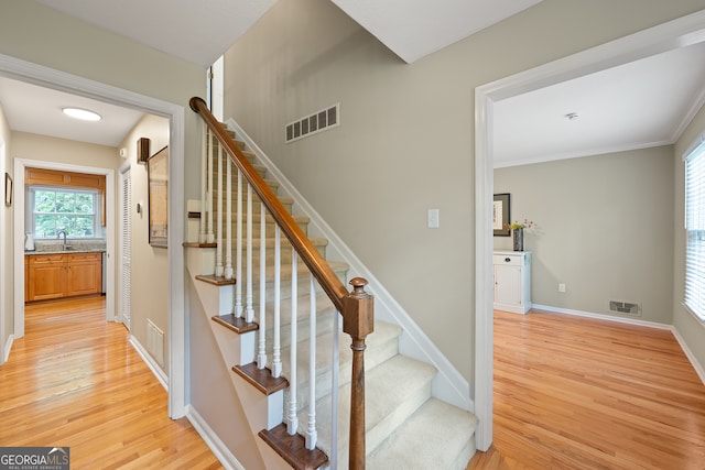 stairway featuring wood finished floors, baseboards, and crown molding