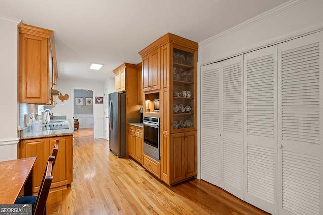 kitchen with stainless steel appliances, crown molding, light wood-type flooring, light stone counters, and glass insert cabinets