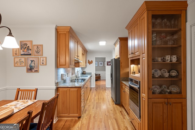 kitchen featuring stainless steel appliances, light wood-style flooring, light stone counters, under cabinet range hood, and decorative backsplash