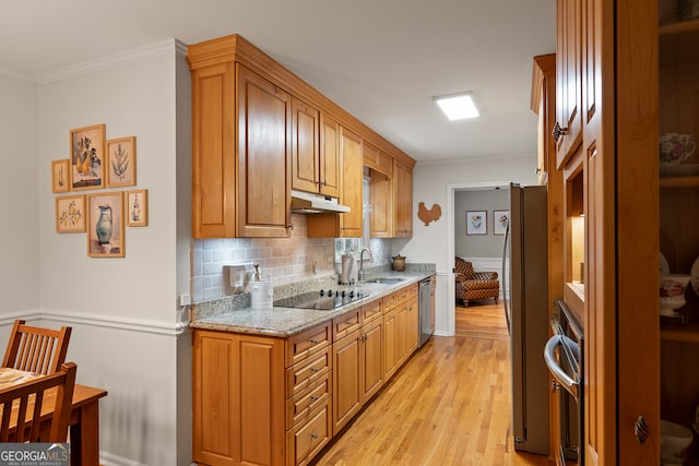 kitchen with under cabinet range hood, appliances with stainless steel finishes, a sink, crown molding, and light wood finished floors