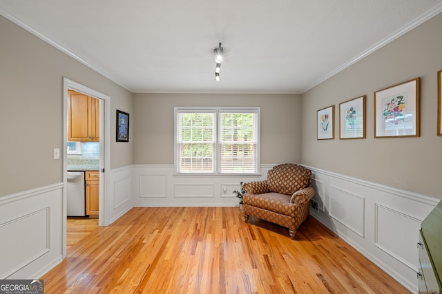 sitting room featuring light wood-style flooring, crown molding, a wainscoted wall, a decorative wall, and track lighting
