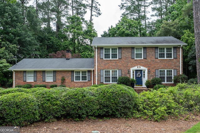 colonial inspired home featuring brick siding and a chimney