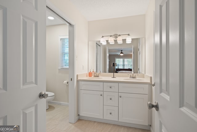 full bath with connected bathroom, double vanity, toilet, ceiling fan, and baseboards