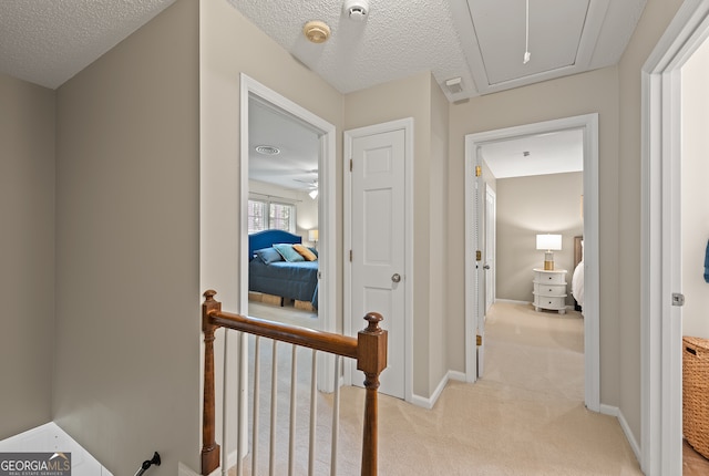 corridor with light colored carpet, attic access, a textured ceiling, and baseboards