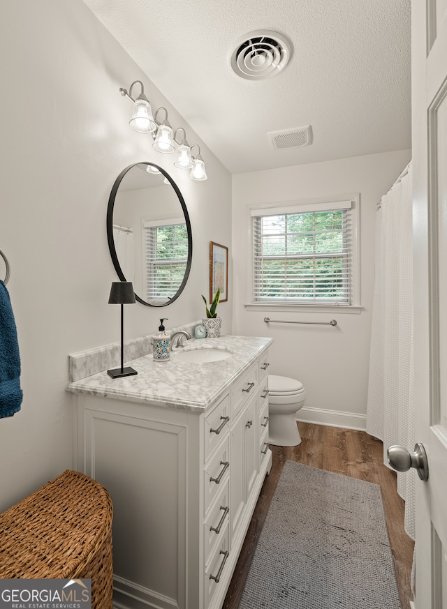 full bath featuring wood finished floors, toilet, vanity, a textured ceiling, and baseboards