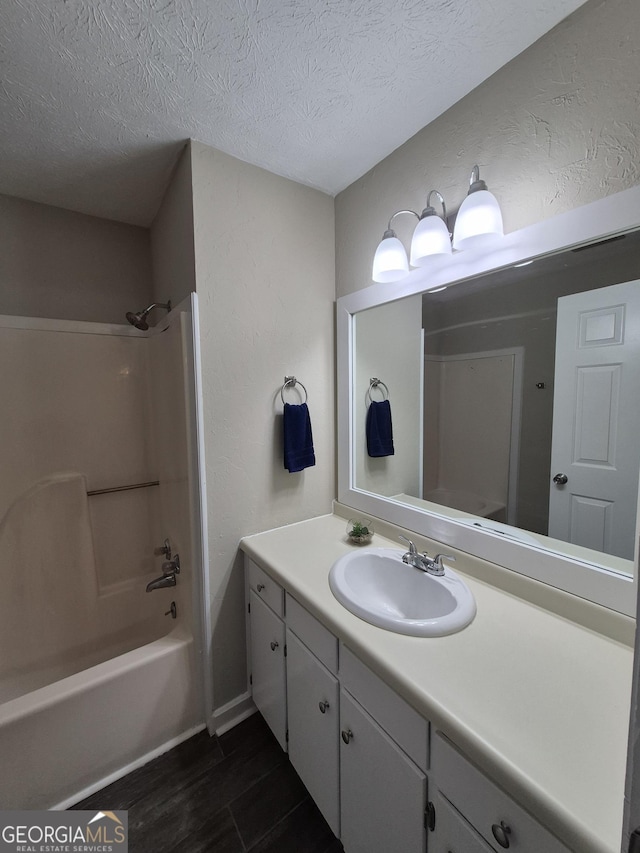 full bathroom with a textured ceiling, vanity, wood finished floors, tub / shower combination, and a textured wall
