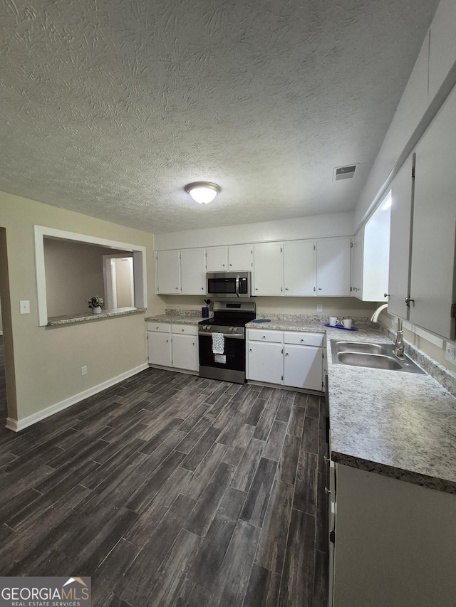 kitchen featuring stainless steel appliances, a sink, dark wood-type flooring, white cabinetry, and baseboards