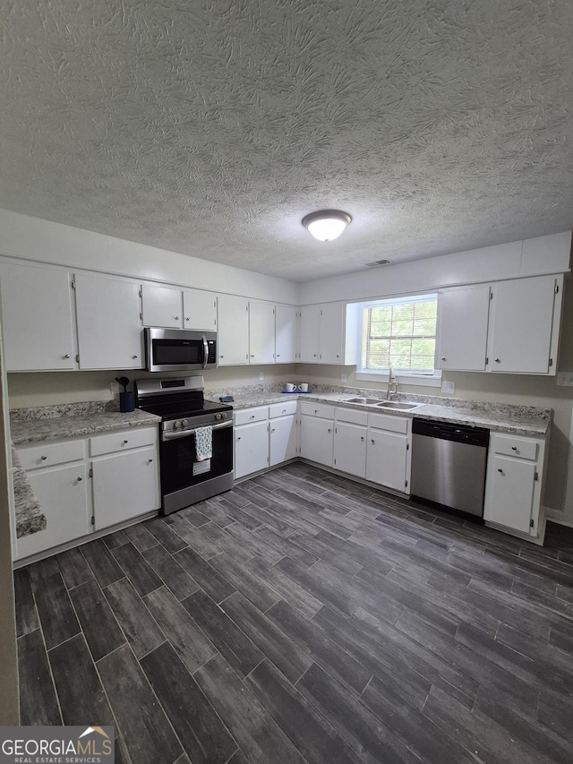 kitchen with appliances with stainless steel finishes, a sink, dark wood-type flooring, white cabinets, and a textured ceiling