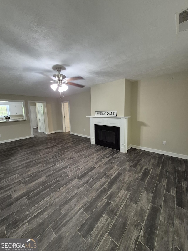 unfurnished living room featuring dark wood finished floors, baseboards, a fireplace, a ceiling fan, and a textured ceiling