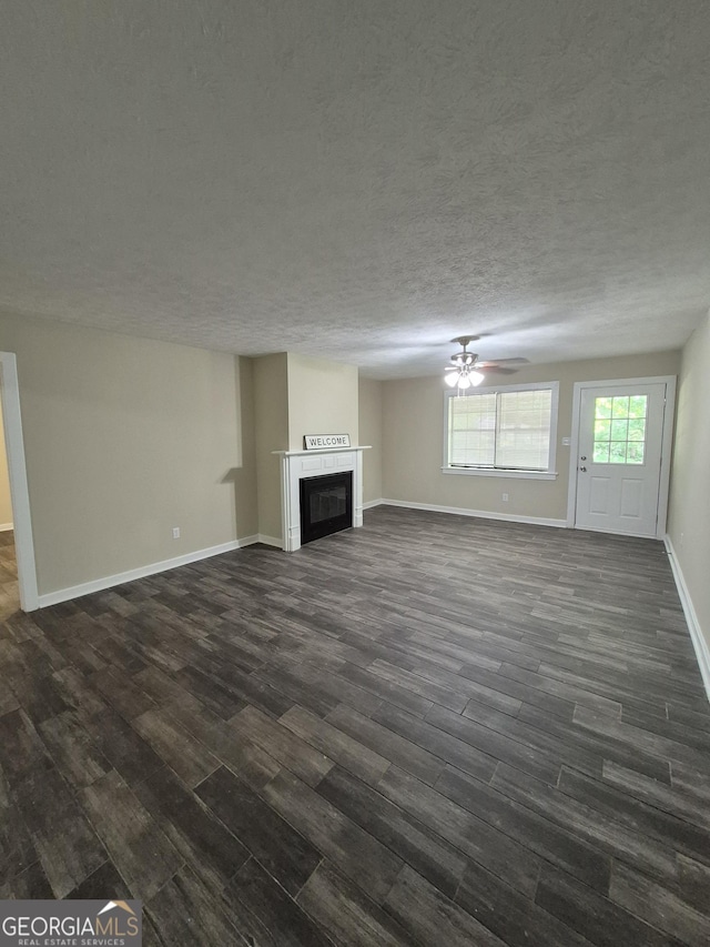 unfurnished living room with dark wood finished floors, a ceiling fan, baseboards, a fireplace, and a textured ceiling