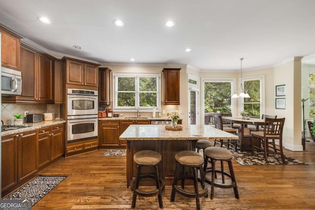 kitchen featuring appliances with stainless steel finishes, a sink, ornamental molding, tasteful backsplash, and a kitchen breakfast bar