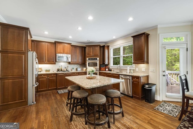 kitchen with stainless steel appliances, dark wood-type flooring, a center island, backsplash, and ornamental molding