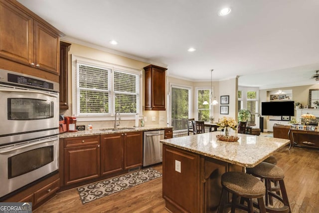 kitchen with appliances with stainless steel finishes, a sink, ornamental molding, light stone countertops, and a kitchen island