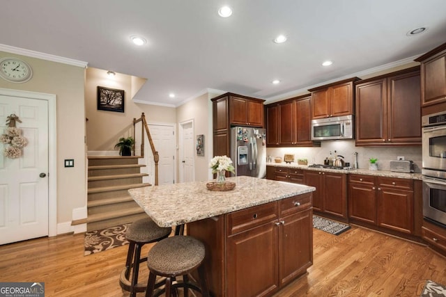 kitchen featuring appliances with stainless steel finishes, a kitchen breakfast bar, crown molding, a kitchen island, and light stone countertops