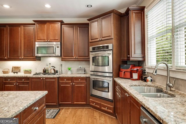 kitchen featuring stainless steel appliances, a sink, light wood-type flooring, light stone counters, and tasteful backsplash