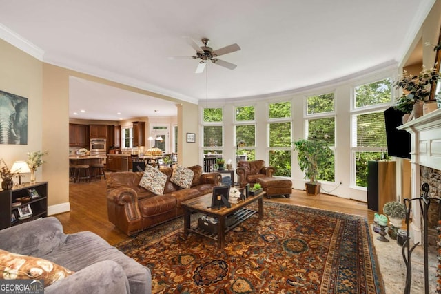 living area with crown molding, ceiling fan, wood finished floors, and a fireplace