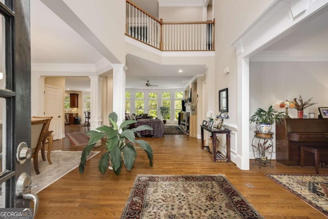 entrance foyer featuring decorative columns, a ceiling fan, wood finished floors, crown molding, and a high ceiling
