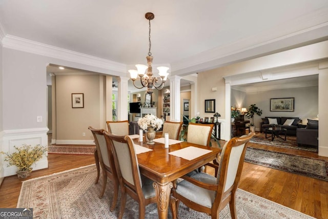 dining room with crown molding, a chandelier, wood finished floors, and ornate columns