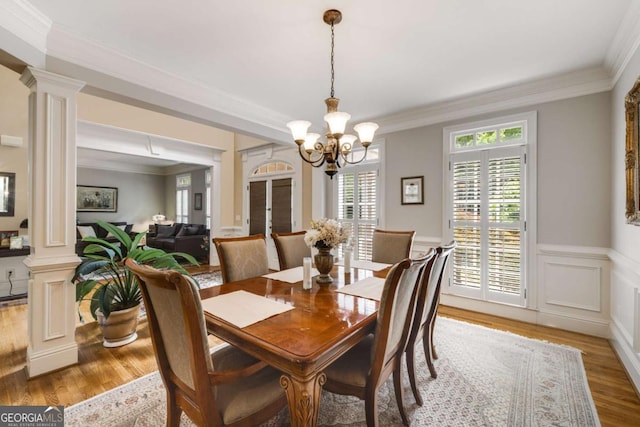 dining area featuring decorative columns, light wood-style floors, a chandelier, ornamental molding, and wainscoting