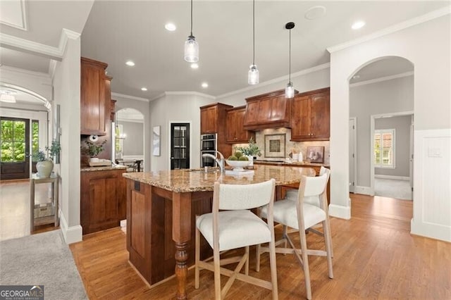 1286 Whisper Cove Dr, Buford, GA 30518 - kitchen with arched walkways, crown molding, stainless steel double oven, light wood-style flooring, and tasteful backsplash