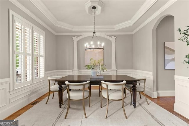 1286 Whisper Cove Dr, Buford, GA 30518 - dining area with decorative columns, a tray ceiling, light wood-style floors, a wainscoted wall, and arched walkways