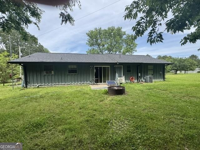 back of house with board and batten siding, a fire pit, a lawn, and central AC unit
