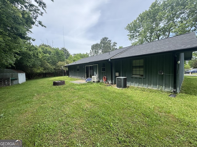 back of property featuring board and batten siding, an outdoor fire pit, cooling unit, and a yard