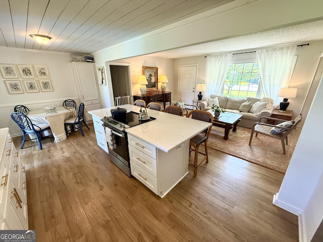 3095 Holbrook Dr SW, Marietta, GA 30060 - kitchen with stainless steel range with electric stovetop, a kitchen bar, white cabinetry, a center island, and wood finished floors